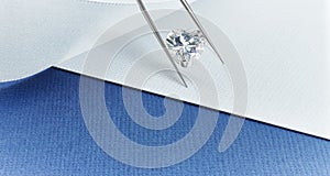 Heart Shaped Diamond Held in Tweezers Over Background in Blue and White photo