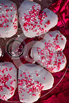 Heart-shaped donuts with tiny red heart sprinkles on clear glass cake stand