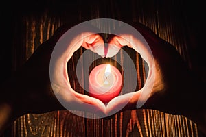 Heart-shaped female hands around  burning candle