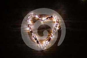 A heart shaped figure laid out light LED garland on vintage brown wooden board. Heart made of LED rice lights. Concept of