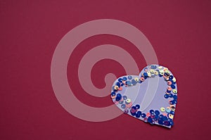 Heart shaped frame made of shiny sequins on a blue background. Festive texture for Valentines Day, Mothers Day, Womens