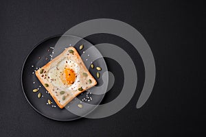 Heart shaped fried egg in bread toast with sesame seeds, flax seeds and pumpkin seeds on a black plate