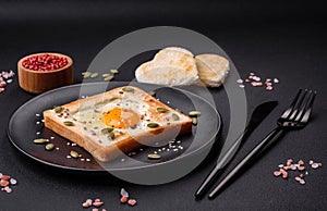 Heart shaped fried egg in bread toast with sesame seeds, flax seeds and pumpkin seeds on a black plate