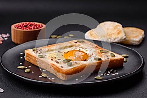 Heart shaped fried egg in bread toast with sesame seeds, flax seeds and pumpkin seeds on a black plate