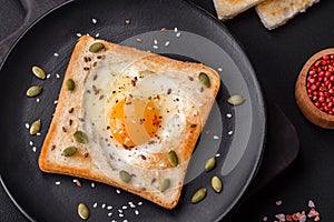 Heart shaped fried egg in bread toast with sesame seeds, flax seeds and pumpkin seeds on a black plate