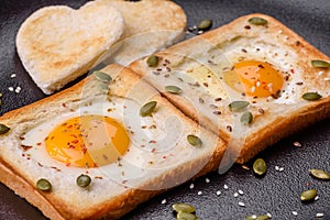 Heart shaped fried egg in bread toast with sesame seeds, flax seeds and pumpkin seeds on a black plate