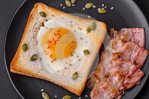 Heart shaped fried egg in bread toast with sesame seeds, flax seeds and pumpkin seeds on a black plate