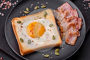 Heart shaped fried egg in bread toast with sesame seeds, flax seeds and pumpkin seeds on a black plate