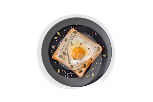 Heart shaped fried egg in bread toast with sesame seeds, flax seeds and pumpkin seeds on a black plate