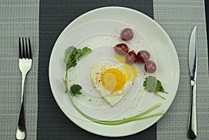 Heart-shaped fried egg, cherry tomatoes, top view of knife and fork, nutrient breakfast, healthy eating