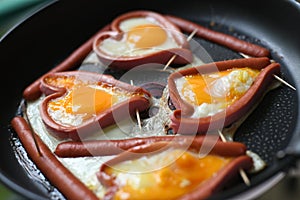 Heart shaped fried eggs in sausages in a frying pan