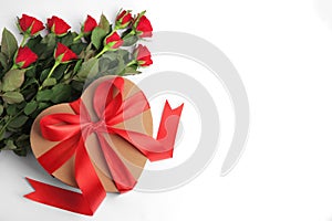 Heart shaped gift box with bow and beautiful red roses on white background, flat lay. Space for text