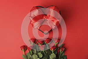 Heart shaped gift box with bow and beautiful roses on red background, flat lay