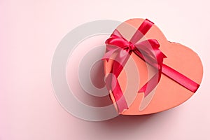 Heart shaped gift box with red ribbon bow on pastel pink background with copy space. Happy Valentines day, Mothers day, birthday