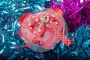Heart shaped gift box with ribbon and bow on a tinsel background