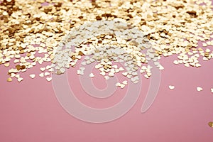 Heart shaped golden confetti on a pink background