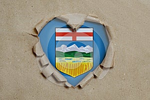 Heart shaped hole torn through paper, showing Alberta flag