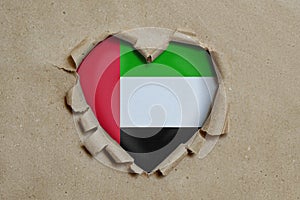 Heart shaped hole torn through paper, showing United Arab Emirates flag