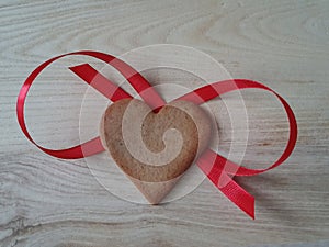 heart-shaped homemade gingerbread decorated with red ribbon on a light wooden background, Valentine's Day, greeting card