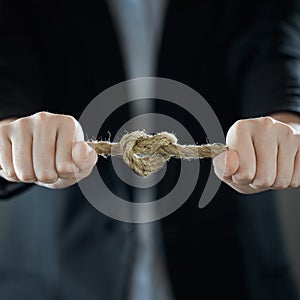 A heart-shaped knot. The businessman& x27;s hands tighten the rope knot against background of suit in blur. The concept