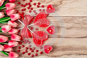 Heart shaped lollipops on wooden background with heart shaped candles lined with tulips flowers. Festive background