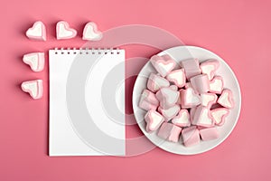 Heart-shaped marshmallow, white notepad, flamingo pen on a pink background Happy Valentine`s Day