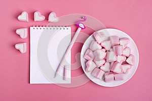 Heart-shaped marshmallow, white notepad, flamingo pen on a pink background Happy Valentine`s Day