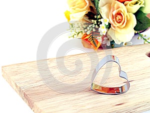 heart shaped metal cookies cutter on wooden cutting board with bouquet artificial fabric flower isolated on white background