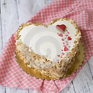 Heart shaped napoleon cake decorated with cookies in the form of red hearts on white wooden table. Valentine`s Day Cake. Copy