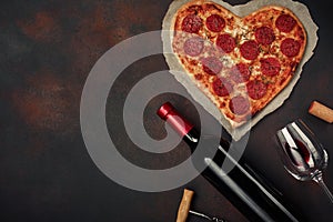 Heart shaped pizza with mozzarella, sausagered with a bottle of wine and wineglas on rusty background