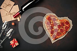 Heart shaped pizza with mozzarella, sausagered, wine bottle, two wineglass, gift box on rusty background