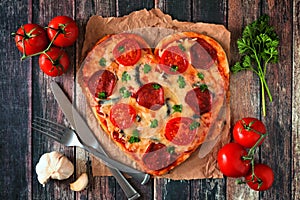 Heart shaped pizza for Valentines Day over dark wood, table scene with ingredients