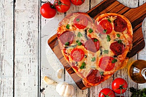 Heart shaped pizza for Valentines Day over white wood, above view, side border table scene