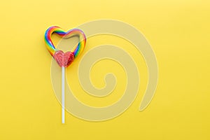 Heart shaped rainbow swirl lollipop on bright yellow solid background