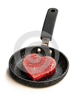 Heart shaped raw beef meat on small frying pan isolated on white. Healthy lifestyle or organic food concept for meat lovers