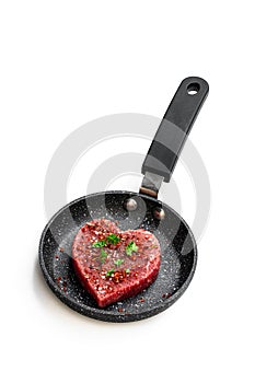 Heart shaped raw beef meat with spices on small frying pan isolated on white. Healthy lifestyle or organic food concept for meat