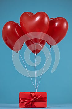 Heart-shaped red balloons attached to a wrapped gift with a red ribbon on a blue background