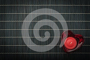 Heart-shaped red candlestick with candle on a bamboo placemat