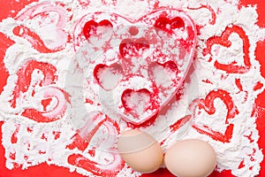 Heart-shaped red silicone mold, eggs and sprinkled flour on a red background.