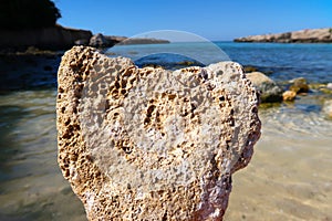 A heart shaped rock, eroded limestone with sea in the background - summer holiday vacations concept - Italy, Apulia, Monopoli