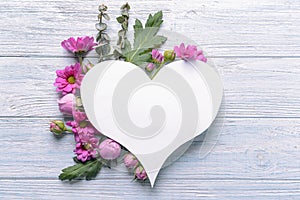 Heart shaped sheet of paper with beautiful flowers and leaves on light wooden background