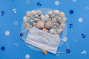 Heart-shaped shells with a medical mask on a blue background. Marine theme. top view