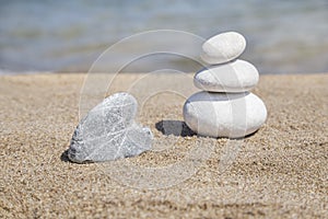 Heart shaped stone and stack of pebbles on balance on sandy beach