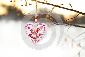 Heart shaped Valentines or Christmas decoration toy hanging on the tree branch with snow on the background