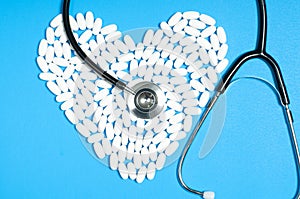 Heart of white pills and stethoscope on blue background