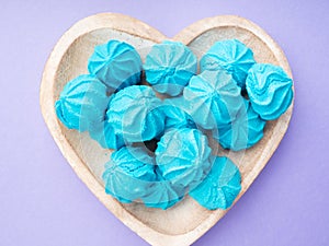 Heart shaped wooden dish with blue sweet meringues on purple