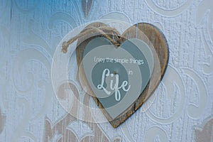 Heart-shaped wooden frame sign hang on the wall, which reads Enjoy the simple things in life