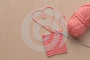 Heart Shaped Yarn and Crochet handmade square pattern, pink yarn coil, hook, knitting crocheting top view on a wooden background photo