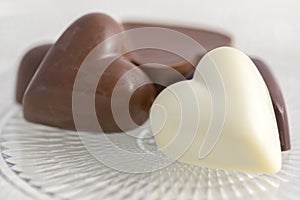 Heart shapped chocolate sweets, brown and white color, transparent retro plate with pralines