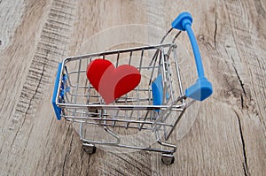 Heart in a shopping cart on a wooden background. Close-up.